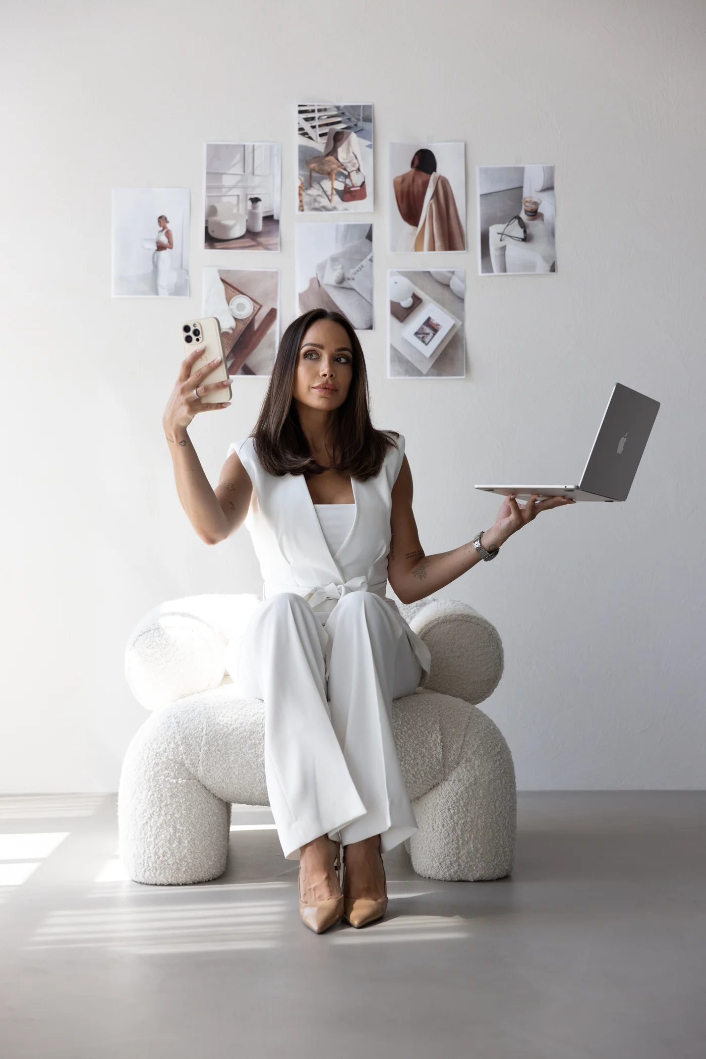 Noemi balancing a laptop and phone in a white suit